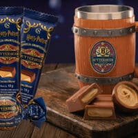 Embalagens e uma caneca de madeira com cerveja Butterbeer (Cacau Show) inspirada em Harry Potter, sobre mesa