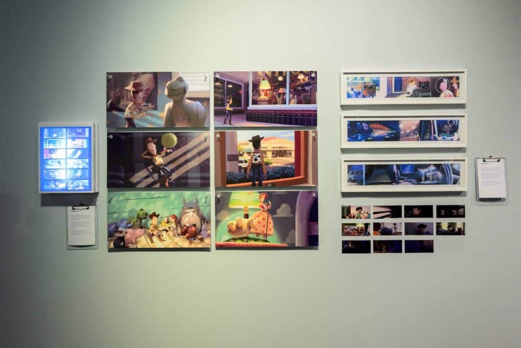 Exposição na galeria apresentando diversas imagens emolduradas de filmes de animação, incluindo personagens e cenas, juntamente com um painel iluminado e folhetos informativos.