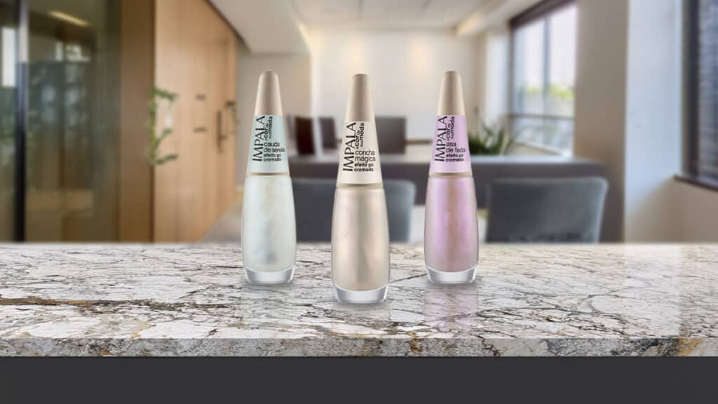 Esmaltes cromados da Impala em frascos na bancada, com cores prateada e rosada ao fundo.