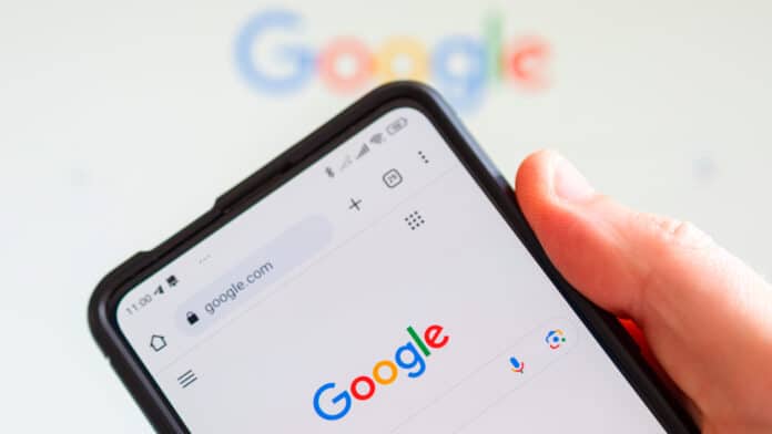 Mão segurando smartphone com tela do Google aberta ao fundo