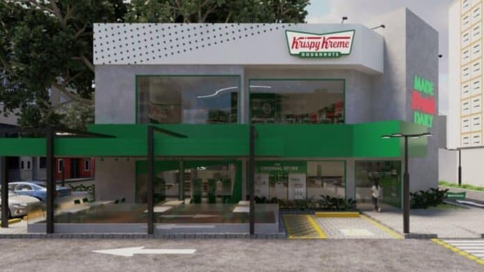 Fachada da Krispy Kreme Donuts em SP, com placa do logo e cobertura verde em frente à rua.