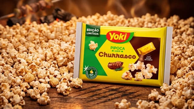 Embalagem de pipoca de micro-ondas Yoki edição limitada sabor Churrasco, cercada por pipocas na mesa.