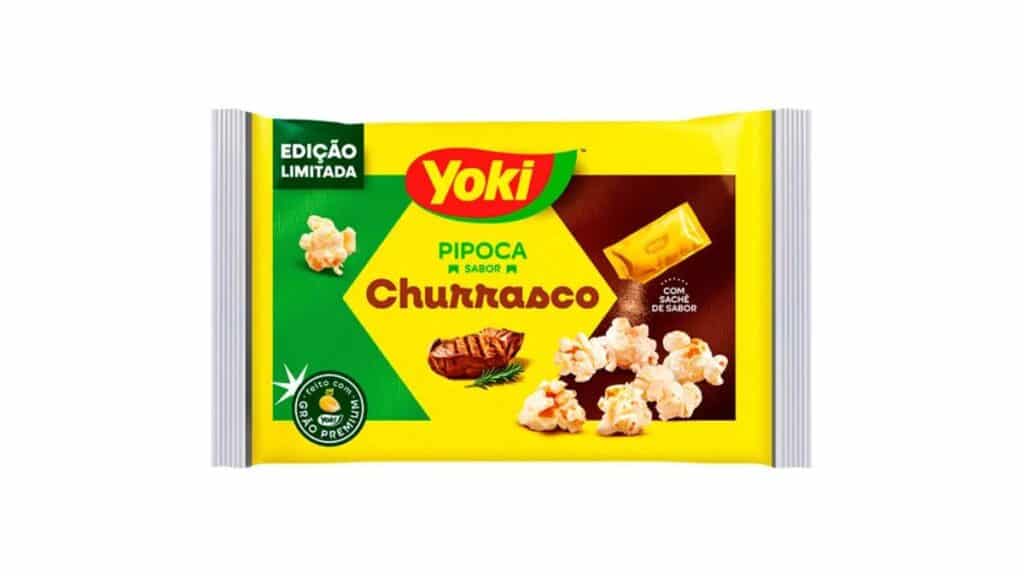 Embalagem da Yoki Pipoca sabor Churrasco, edição limitada para micro-ondas, com imagem de pipoca e pedaços de queijo