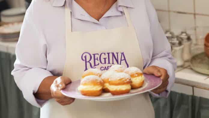 Funcionária do Regina Café segurando prato com sonhos; marca Regina Café visível em avental