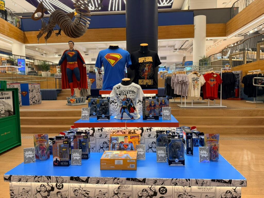 Painel promocional do Superman Day em loja com bonecos, camisetas e produtos da Piticas e Galeria Magalu