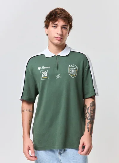 Homem usando camiseta polo verde com zíper frontal e estampa da Copa do Mundo, da coleção Guaraná Antarctica e YouCom.
