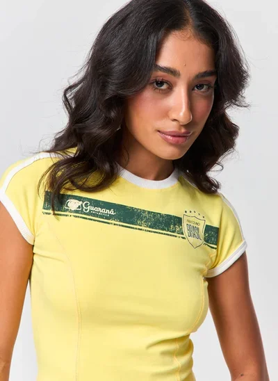 Modelo vestindo blusa amarela com estampa e logotipos da Guaraná Antarctica, em ensaio de moda para a Copa do Mundo.