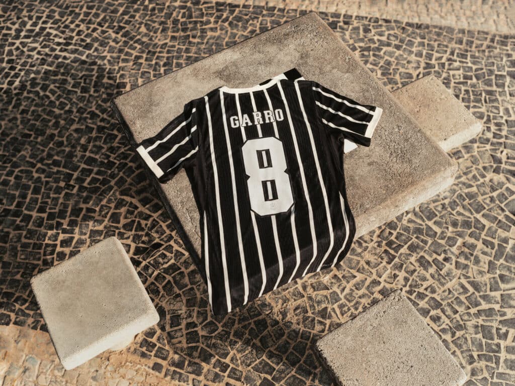 Camisa de futebol preta e branca em listras, de costas, com número 8 e escudo de GARR0 sobre piso de pedra.
