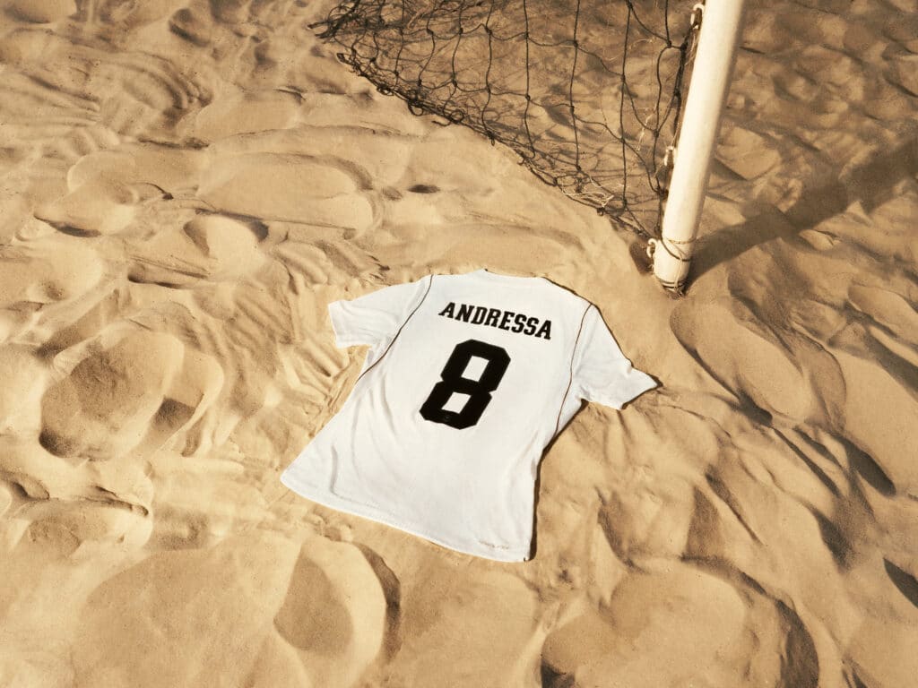 Camisa de futebol branca com o nome “ANDRESSA” e o número 8 nas costas sobre tecido estampado.