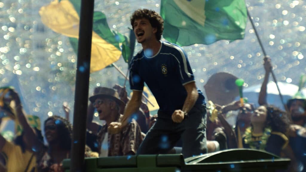 Jovem celebra no palco em evento com bandeiras do Brasil e iluminação festiva, cenário da campanha Volkswagen “Sonhos” para a Copa do Mundo.