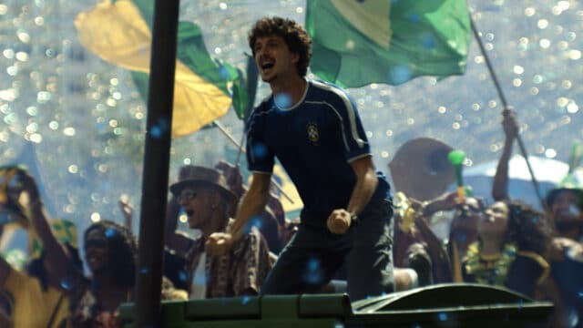 Jovem celebra no palco em evento com bandeiras do Brasil e iluminação festiva, cenário da campanha Volkswagen “Sonhos” para a Copa do Mundo.