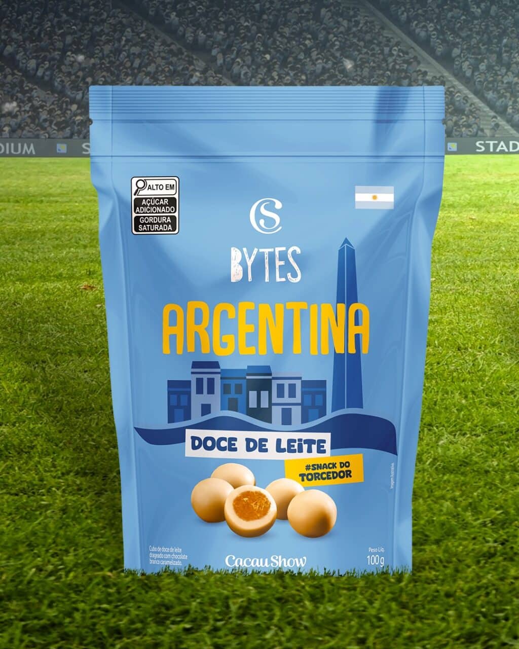 Embalagem de snack da Cacau Show Bytes Argentina, sabor doce de leite, no gramado de estádio.