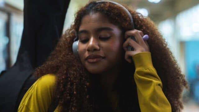 Mulher com fones de ouvido, falando ao telefone com tela amarela, em contexto de música e experiência digital com Deezer e TIM.