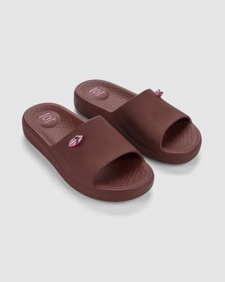 Chinelos marrons de collab inspirada no chocolate, estilo slide, com detalhe no cabedal e logo discretos