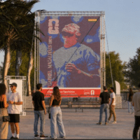 Pessoas em área externa observam um grande painel de figurinhas da Coca-Cola
