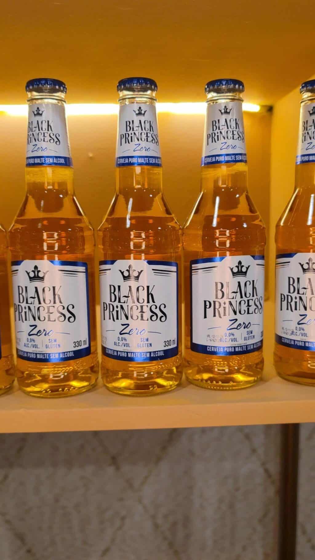 Garrafinhas da bebida Black Princess Zero em exposição, com rótulos visíveis, em ambiente amarelo.