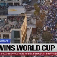 Cena externa com multidão e tela da Fox Sports com texto “USA WINS WORLD CUP” em campanha da Copa do Mundo.