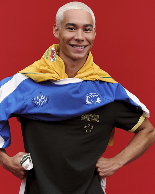 Modelo com jaqueta colorida estilo futebol, azul e amarela, em fundo vermelho, em collab Renner e Guaraná Antarctica.