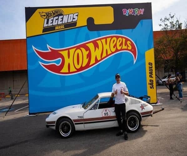 Carro customizado Hot Wheels Legends Brasil em evento, com pessoa ao lado e faixa “Hot Wheels Legends” ao fundo.
