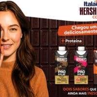 Mulher segura embalagem de bebida Italac + Hershey’s e, ao fundo, a linha ProPlay Proteína e outros sabores da collab