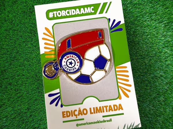 Embalagem American Cookies edição limitada com tema de futebol na grama, com selo “Torcida AMC” e ícone de bola.