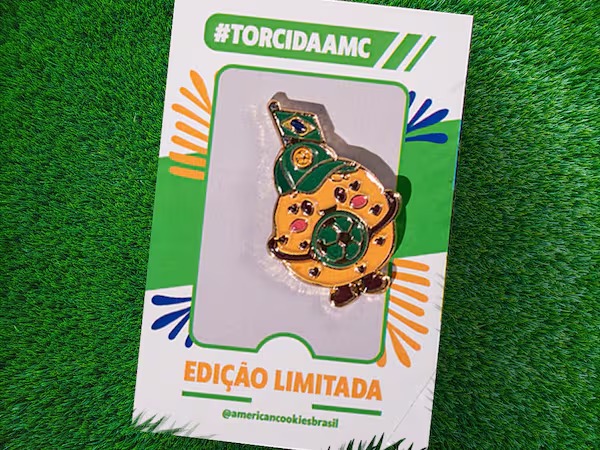 Embalagem de American Cookies na grama, com pino e texto #TORCIDAAMC e “EDIÇÃO LIMITADA” ao fundo