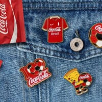 Pins colecionáveis da Coca-Cola na Copa do Mundo em uma jaqueta jeans, incluindo emblemas de futebol e acessórios de tema esportivo.
