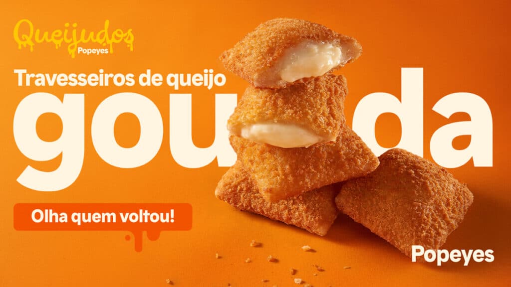 Popeyes retorna Travesseiro de Queijo Gouda Popeyes anuncia retorno dos travesseiros de queijo gouda: imagem com salgados empilhados e fundo laranja.
