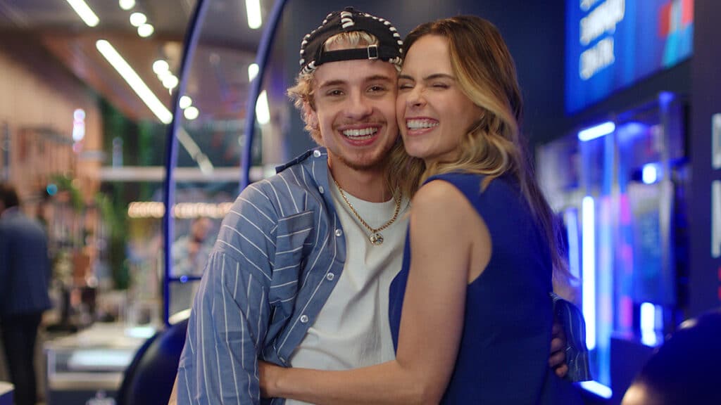 Ana Paula Renault e Juliano Floss em clima de abraço, sorrindo, em cenário de campanha publicitária da TIM.