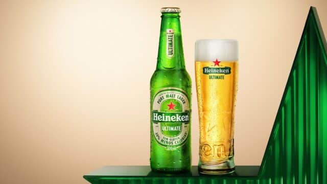 Garrafa e copo Heineken Ultimate com rótulo verde e cerveja dourada, em fundo claro