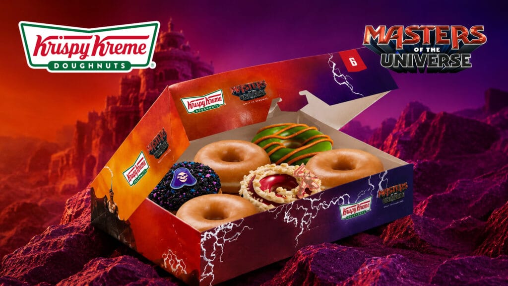 Krispy Kreme Mestres do Universo: donuts temáticos em caixa Caixa de donuts Krispy Kreme temáticos de Mestres do Universo, com três donuts decorados em cenário roxo e vermelho.
