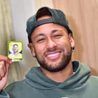 Homem sorrindo segurando uma figurinha dourada do Neymar Jr. em edição limitada do Mercado Livre.