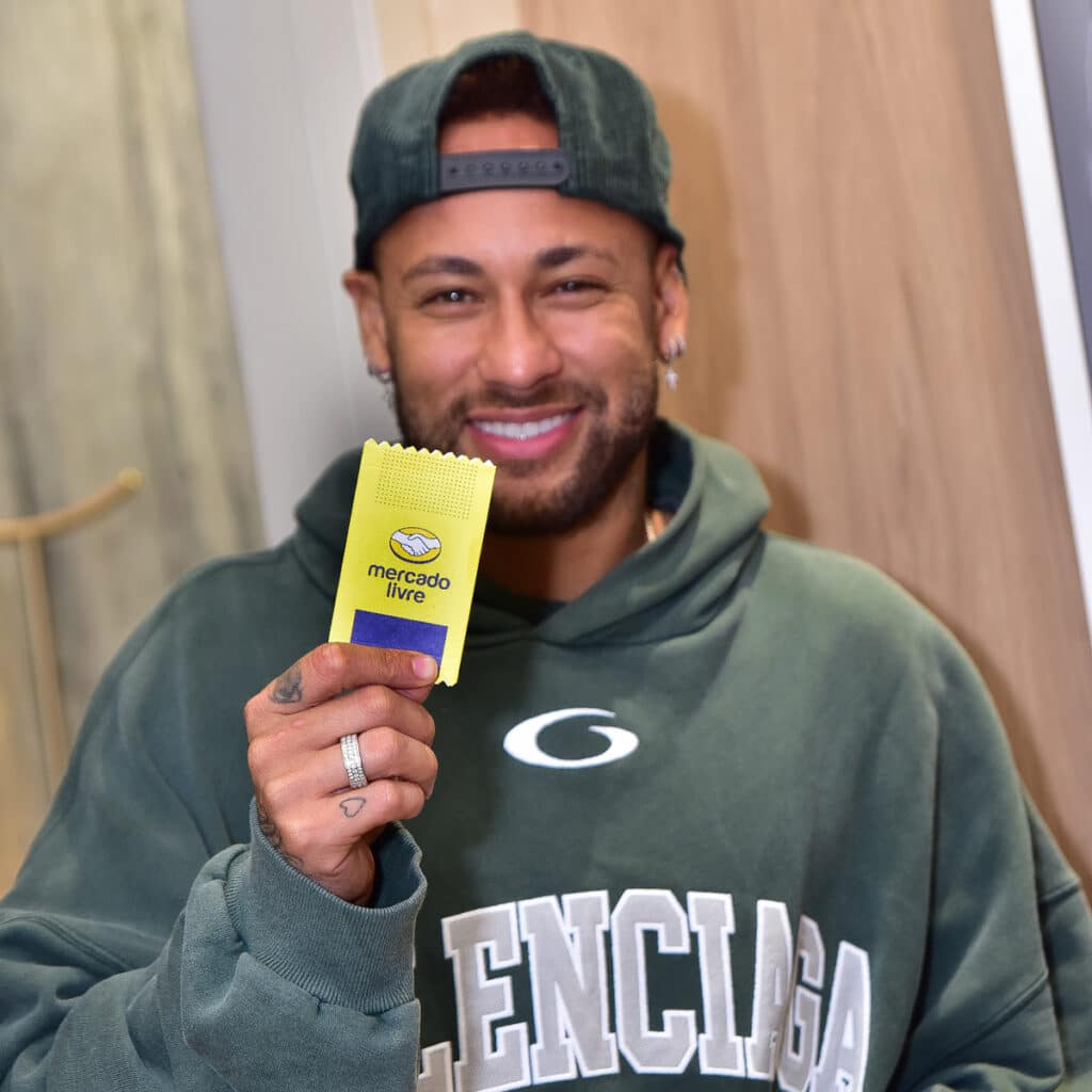 Neymar Jr. em foto segurando figurinha/adesivo dourado do Mercado Livre com Neymar ao lado.