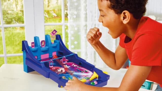 Criança brincando com um pinball temático do Super Mario Galaxy, da Epoch Magia, sobre uma mesa branca