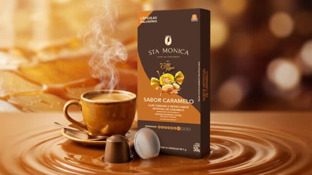 Embalagem de cápsulas Sta Monica sabor caramelo ao lado de xícara de café, com doce e gota de café ao fundo.