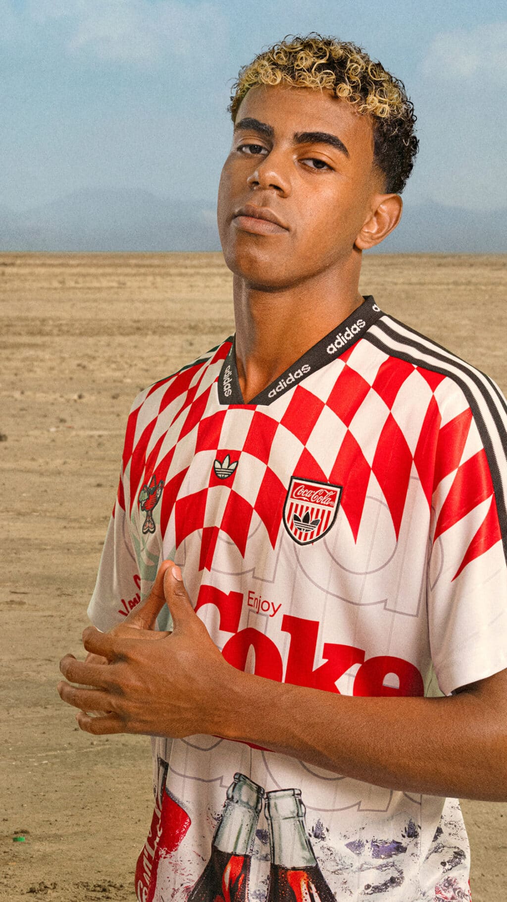Modelo com camisa adidas x Coca-Cola listrada vermelha e branca, em campo aberto, com colarinho listrado