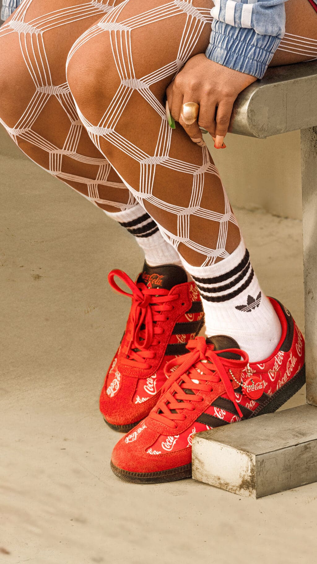 Tênis vermelho Adidas Originals x Coca-Cola com cadarço vermelho, usados com meia listrada e calça jeans, em cenário externo