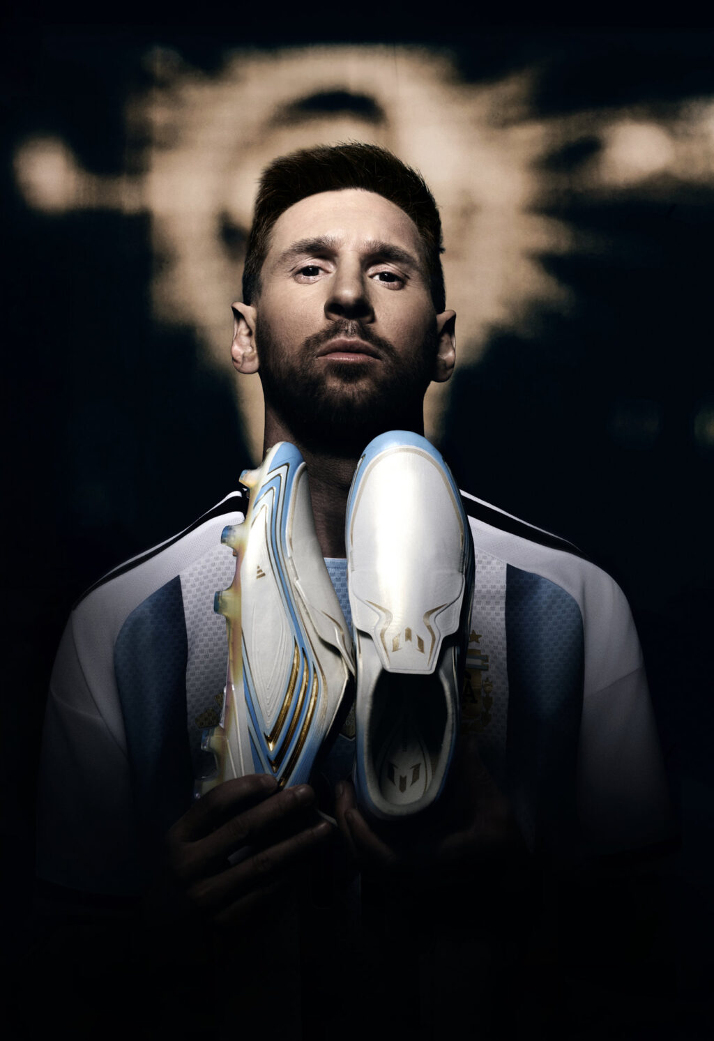 Lionel Messi segurando uma chuteira branca e azul da Adidas em fundo escuro, em campanha da coleção “El Último Tango”.