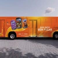 Ônibus laranja da ativação Fanta com campanhas e embalagens na lateral, em cenário aberto ao ar livre.