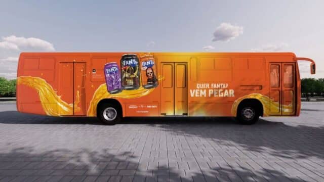 Ônibus laranja da ativação Fanta com campanhas e embalagens na lateral, em cenário aberto ao ar livre.