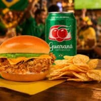 Sanduíche Aussie Hexa Chicken com frango crocante, acompanhado de batatas e refrigerante Guaraná Antarctica em clima de torcida.