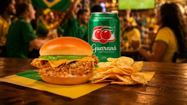 Sanduíche Aussie Hexa Chicken com frango crocante, acompanhado de batatas e refrigerante Guaraná Antarctica em clima de torcida.
