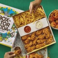 Box da Torcida KFC com frango empanado e porção de fritas sendo compartilhado sobre fundo verde.