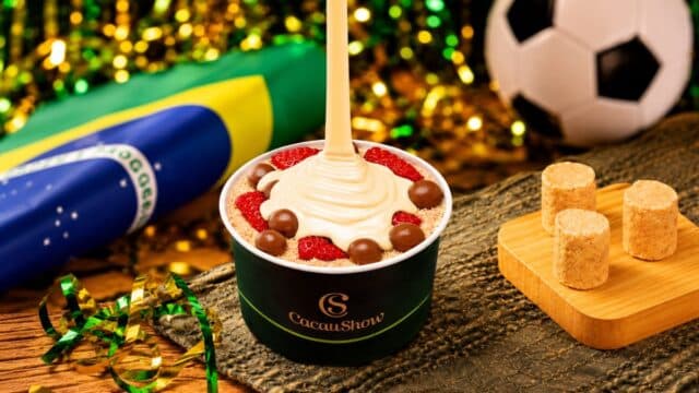 Copo de cacau com fondue de chocolate branco e gotas, com morangos, ao lado de bola e mesa temática de futebol