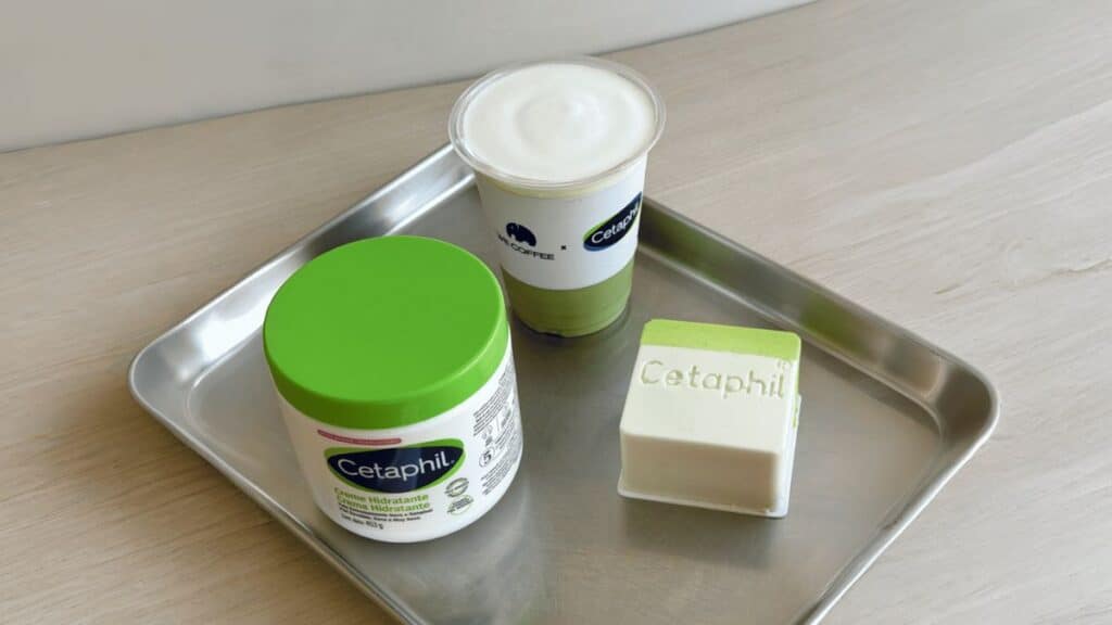 Produtos Cetaphil em bandeja, com pote verde, copo e sabonete em barra, sugerindo colaboração com café.