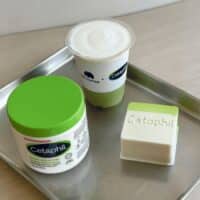 Produtos Cetaphil em bandeja, com pote verde, copo e sabonete em barra, sugerindo colaboração com café.