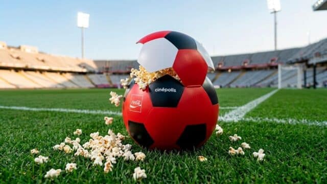 Balde de pipoca em formato de bola de futebol Cinépolis e Coca-Cola sobre grama, em estádio