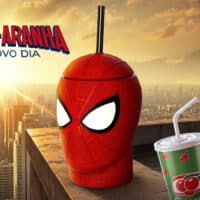 Copo em formato do Homem-Aranha ao lado de copo UCI com bebida, em cenário com a cidade ao fundo.