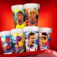 Copos colecionáveis do McDonald’s para a Copa do Mundo FIFA 2026 com ilustrações de jogadores, em fundo vermelho