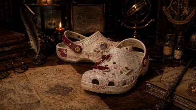 Crocs modelo inspirado no Mapa do Maroto, com estampa do mapa e cadarço bege, ao lado de livros e itens mágicos
